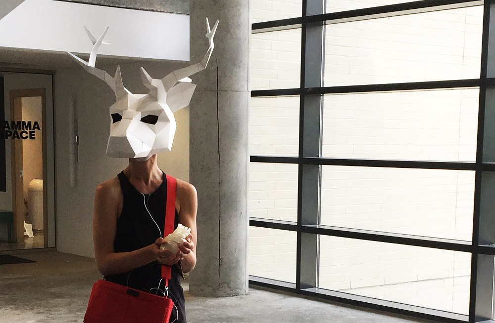 A woman in a hallway wearing a geometric white deer head mask
